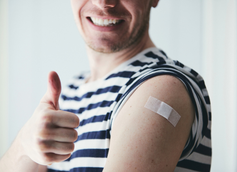 happy young man showing thumb up and his arm after vaccination